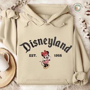 A beige hoodie with the text "Disneyland EST. 1955" and a Minnie Mouse graphic, along with a wooden tray and some white cotton balls.
