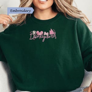 A woman wearing a green sweater with the text "Disneyworld" embroidered on it.