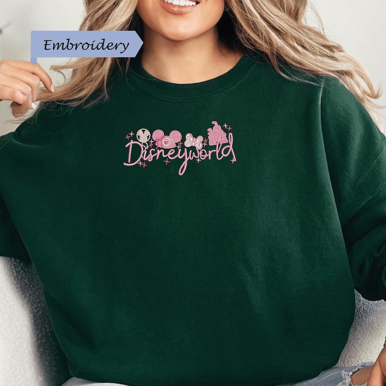 A woman wearing a green sweater with the text "Disneyworld" embroidered on it.