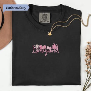 a black t-shirt with a Disney World logo embroidered on it, along with a gold necklace and a hat.