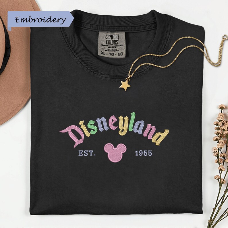 a black t-shirt with a Disneyland logo and text, along with a necklace and some flowers.