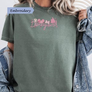 A person wearing a green t-shirt with the text "Disneyworld" embroidered on it, along with various Disney-themed graphics.