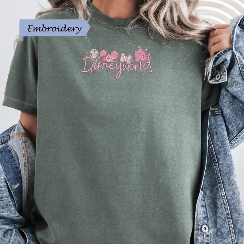 A person wearing a green t-shirt with the text "Disneyworld" embroidered on it, along with various Disney-themed graphics.