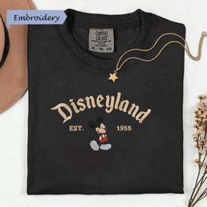 a black t-shirt with a Disney Mickey Mouse embroidered on it, along with a necklace and some flowers.