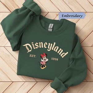 A green sweater with the text "Disneyland EST. 1955" and an embroidered Minnie Mouse character printed on it.