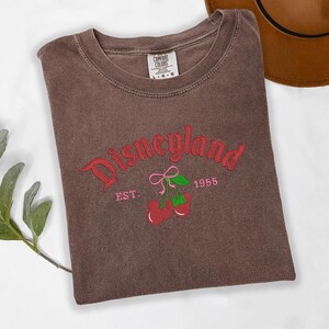A brown t-shirt with the text "Disneyland EST. 1955" printed on it, along with a graphic of cherries.