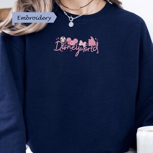 A person wearing a navy blue sweater with the text "Disneyworld" embroidered on it.