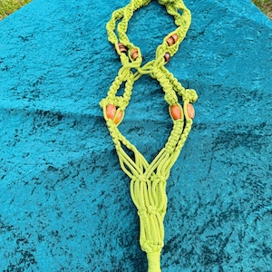 May include: Lime green macrame plant hanger with wooden beads. The plant holder has a metal ring at the top for hanging and a tassel at the bottom. The macrame is knotted in a spiral pattern.