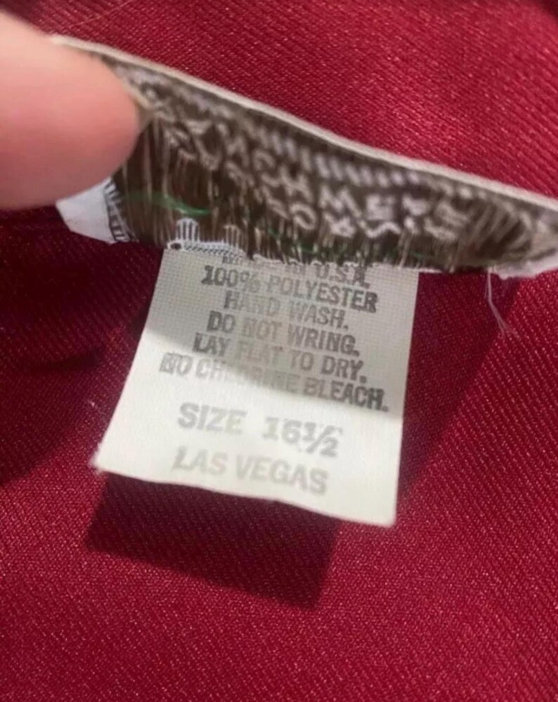 Puede incluir: Etiqueta de cuidado blanca con texto negro. La etiqueta dice: "100% Poli&eacute;ster, Lavar a mano, No escurrir, Secar plano, No usar blanqueador con cloro, Talla 16 1/2, Las Vegas."