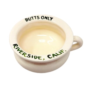 May include: A white ceramic mug with a black handle and the text "But First, Coffee" in a black, handwritten-style font. The mug is on a white surface.