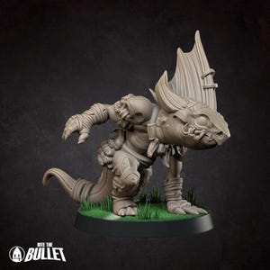 May include: A tan-colored, unpainted miniature figurine of a reptilian creature with a large dorsal fin, textured scales, and wrapped limbs, standing on a circular base with green grass details. The text "BITE THE BULLET" appears in the corner.