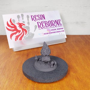 May include: A gray resin miniature of a mushroom creature with a textured cap and a small base. The miniature is on a black circular base.