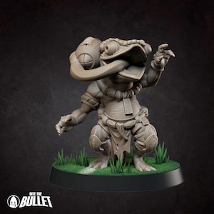 May include: A grey, unpainted miniature figurine of a humanoid frog creature with a long tongue holding a spherical object. The creature wears a necklace, a belt with a hanging cloth, and leg armor. It stands on a circular base with green grass.