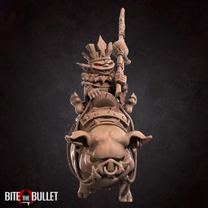 May include: A detailed figurine of a goblin riding a war pig. The goblin is wearing a crown and holding a weapon. The pig has armor and rope detailing. The figurine is a neutral color and has the text "BITE THE BULLET" at the bottom.