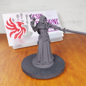 May include: Gray 3D printed miniature of a humanoid figure with tentacles, wearing a hooded robe and holding a sword and a vial. The figure is standing on a round base.