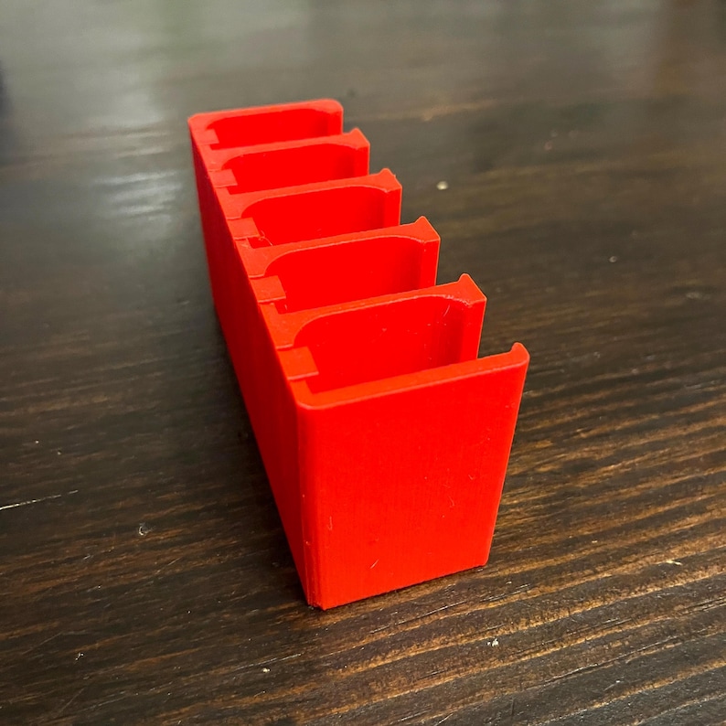 Puede incluir: Un organizador de pl&aacute;stico rojo con cinco ranuras para guardar objetos peque&ntilde;os. El organizador est&aacute; hecho de pl&aacute;stico rojo brillante y tiene un acabado liso y brillante.