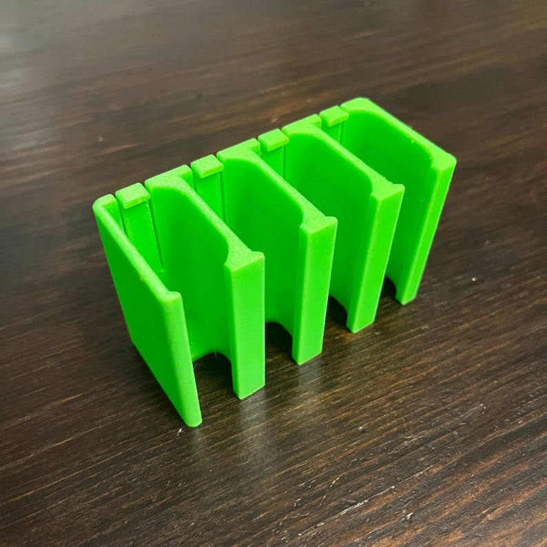 Puede incluir: Un organizador de pl&aacute;stico verde brillante con cuatro compartimentos. El organizador est&aacute; dise&ntilde;ado para guardar objetos peque&ntilde;os, como dados u otros accesorios de juego.