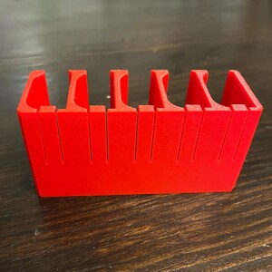 Puede incluir: Un organizador de pl&aacute;stico rojo con cinco compartimentos. El organizador est&aacute; dise&ntilde;ado para guardar objetos peque&ntilde;os, como dados o piezas de juego.