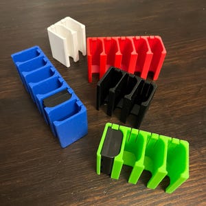 May include: Five different colored plastic card holders. The holders are made of 3D printed plastic and are designed to hold cards vertically. The colors are blue, red, black, white, and green.