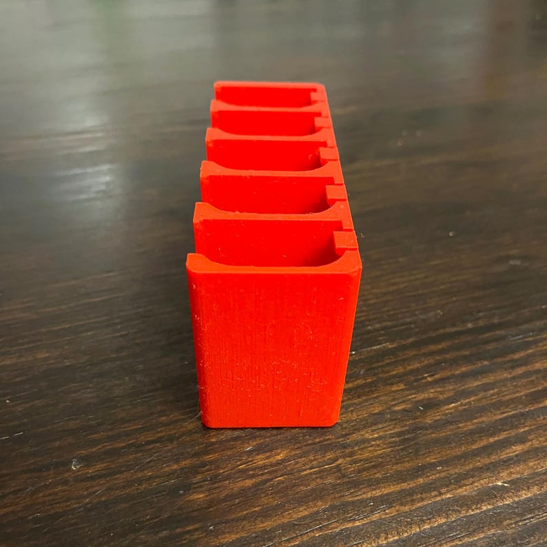 Puede incluir: Un organizador de pl&aacute;stico rojo con seis ranuras para guardar objetos peque&ntilde;os. El organizador est&aacute; hecho de un pl&aacute;stico liso y mate.