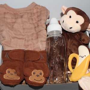 May include: A brown baby gift set with a brown onesie, brown booties, a brown monkey stuffed animal, a clear baby bottle, and a yellow banana teether.