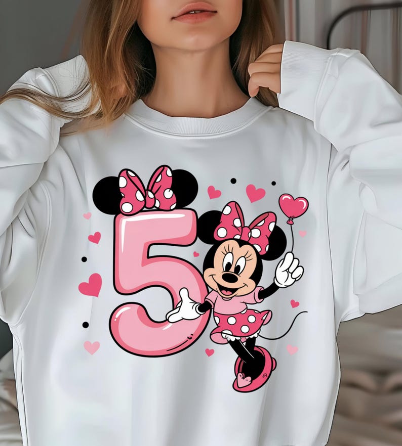 May include: White sweatshirt featuring a pink number 5 with a Minnie Mouse graphic. Minnie Mouse is wearing a pink polka dot dress and holding a heart-shaped balloon. Pink hearts and black dots are scattered around the design.