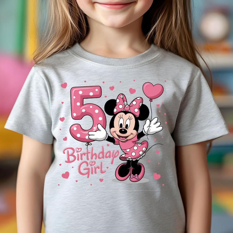 May include: A light gray t-shirt featuring a graphic of Minnie Mouse in a pink polka-dot dress, holding a pink heart-shaped balloon. A large pink number 5 and the words "Birthday Girl" are also on the shirt.