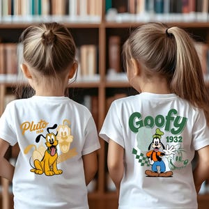 May include: Two white t-shirts with cartoon graphics of Disney characters Pluto and Goofy. The Pluto shirt features a yellow dog with the text "Pluto 1930". The Goofy shirt has a green graphic and the text "Goofy 1932".