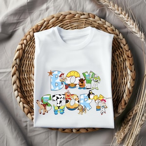 Pu&ograve; includere: T-shirt bianca con la scritta "BOY STORY" in lettere colorate e giocose. Il design incorpora personaggi dei cartoni animati. La maglietta &egrave; esposta su un cestino intrecciato, con spighe di grano sullo sfondo.