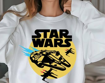 May include: White sweatshirt featuring the text "STAR WARS" in black block letters. Below the text is a yellow circle with a black and yellow illustration of the Millennium Falcon and several black starfighters. Blue streaks emanate from the Falcon.