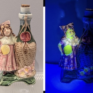 May include: A vintage ceramic bottle with a girl figurine. The bottle has a woven basket design and a cork stopper. The girl wears a pink dress and holds a yellow fan. The base is green with floral accents.