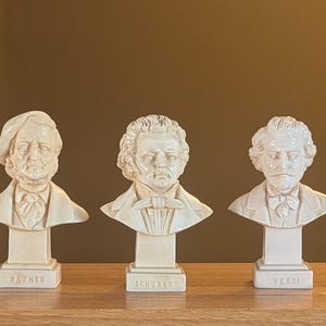 May include: Three off-white busts of composers Wagner, Schubert, and Verdi. Each bust is mounted on a rectangular base with the composer's name. The busts are detailed with facial features, clothing, and hairstyles.