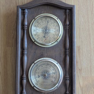 May include: A vintage wooden weather station with a thermometer and barometer. The thermometer displays Fahrenheit, and the barometer shows inches of mercury. An eagle tops the dark brown frame.