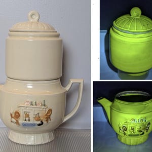 May include: Cream-colored ceramic coffee pot with a lid and a cylindrical top section. The pot features a handle, spout, and a decorative relief scene of a fireplace, spinning wheel, and chair. The design is vintage and likely for serving coffee.