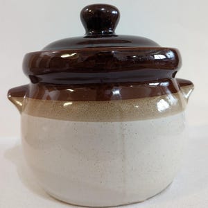 May include: A brown and white ceramic jar with a lid. The jar has a wide mouth and a rounded body. The lid has a knob on top.