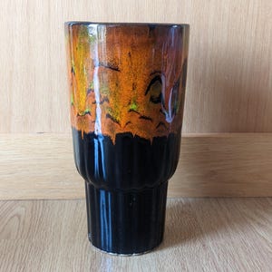 May include: A black and orange ceramic vase with a textured, ribbed design. The vase has a wide mouth and a narrow base.