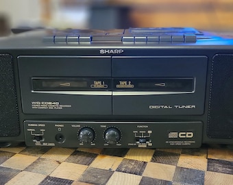 May include: A black Sharp stereo system with a cassette deck, CD player, and digital tuner. The stereo has a silver faceplate with the word "Sharp" in white letters. The cassette deck has two tape slots labelled "Tape 1" and "Tape 2". The CD player has a silver faceplate with the word "CD" in white letters. The digital tuner has a silver faceplate with the word "Digital Tuner" in white letters.