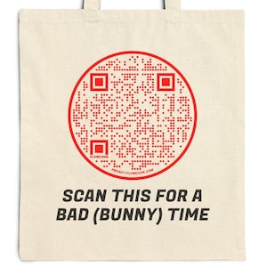 Op de afbeelding: Een witte canvas tote bag met een rode cirkel met daarin een QR-code. De tekst "SCAN THIS FOR A BAD (BUNNY) TIME" staat onder de cirkel.