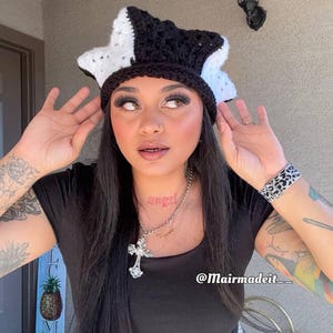 May include: A handmade crochet hat in a star shape, featuring a black and white color scheme. The hat has a textured appearance and is worn on the head. The hat is a unique fashion accessory.