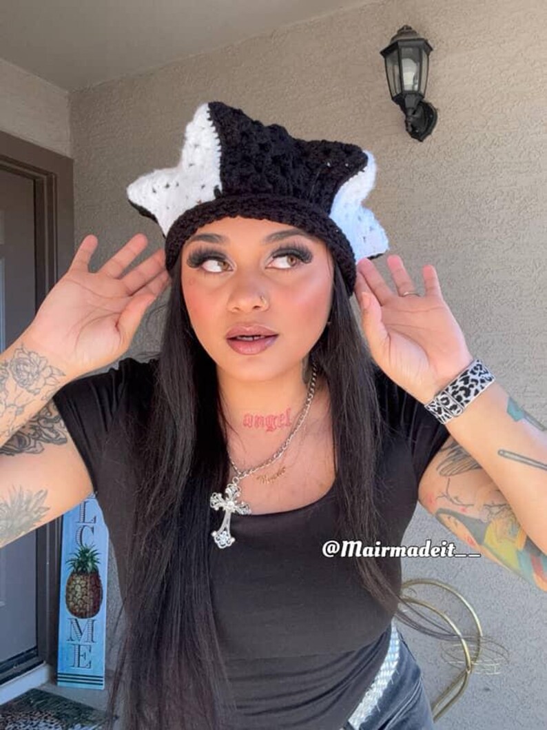 May include: A handmade crochet hat in a star shape, featuring a black and white color scheme. The hat has a textured appearance and is worn on the head. The hat is a unique fashion accessory.