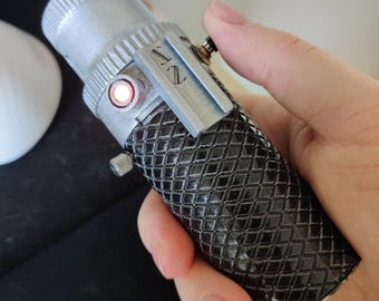 May include: A black and silver lightsaber prop with a red light on the side and a textured grip. The lightsaber is labeled "NZ".