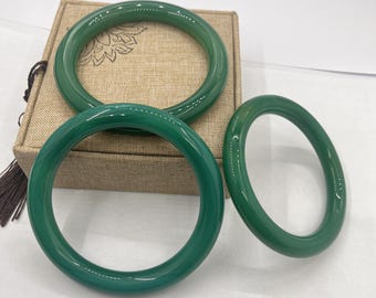 May include: Three green jade bangle bracelets of varying sizes, displayed in a box with a brown fabric lining.