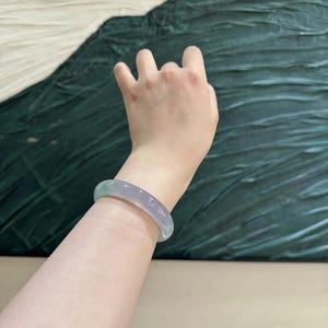 May include: A light green jade bangle bracelet. The bracelet is smooth and polished, with a subtle shimmer.