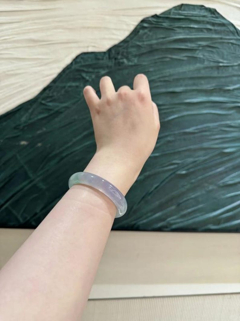 May include: A light green jade bangle bracelet. The bracelet is smooth and polished, with a subtle shimmer.