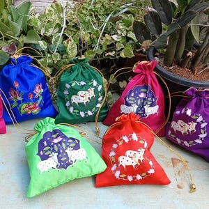 May include: A collection of colorful drawstring bags in various shades, including pink, blue, green, red, and purple. Each bag features an embroidered design with floral or animal motifs. The bags are made of a shiny fabric.