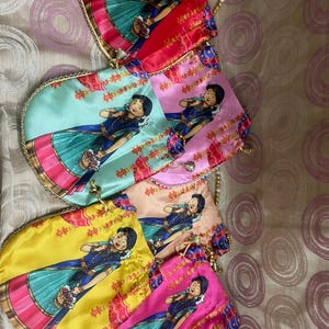 May include: A collection of colorful, fan-shaped purses. Each purse features a cartoon illustration of a woman in traditional Indian attire. The purses are in shades of red, pink, yellow, and teal, with gold beaded handles.