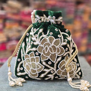 May include: A dark green velvet pouch with intricate floral embroidery in gold and white beads. The drawstring bag features a pearl beaded closure and a matching beaded trim. The pouch is likely used for carrying small items.