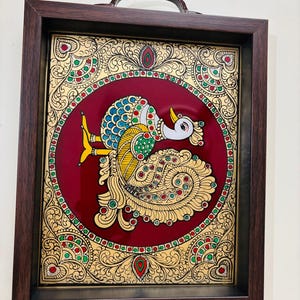May include: A decorative tray with a hand-painted peacock design. The peacock is depicted in vibrant colors against a deep red background, framed by ornate gold detailing. The tray has a dark brown wooden frame and integrated handles.
