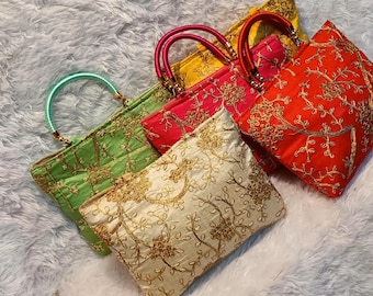 Puede incluir: Una variedad de bolsos bordados en verde, rojo, amarillo y crema. Cada bolso presenta un asa única y intrincados patrones florales dorados, perfectos para llevar lo esencial.