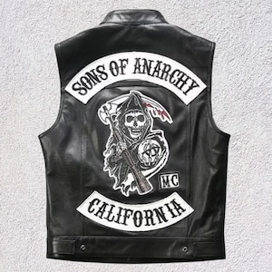 May include: Black leather vest with the "Sons of Anarchy" logo on the back. The logo features a grim reaper with a scythe and a rifle, along with the words "Sons of Anarchy" and "California" in white lettering.